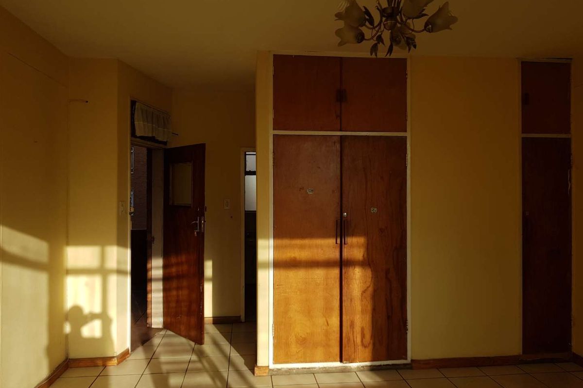 An empty bedroom featuring tiled flooring and built-in wooden cupboards, requiring cosmetic updates to modernize the space.
