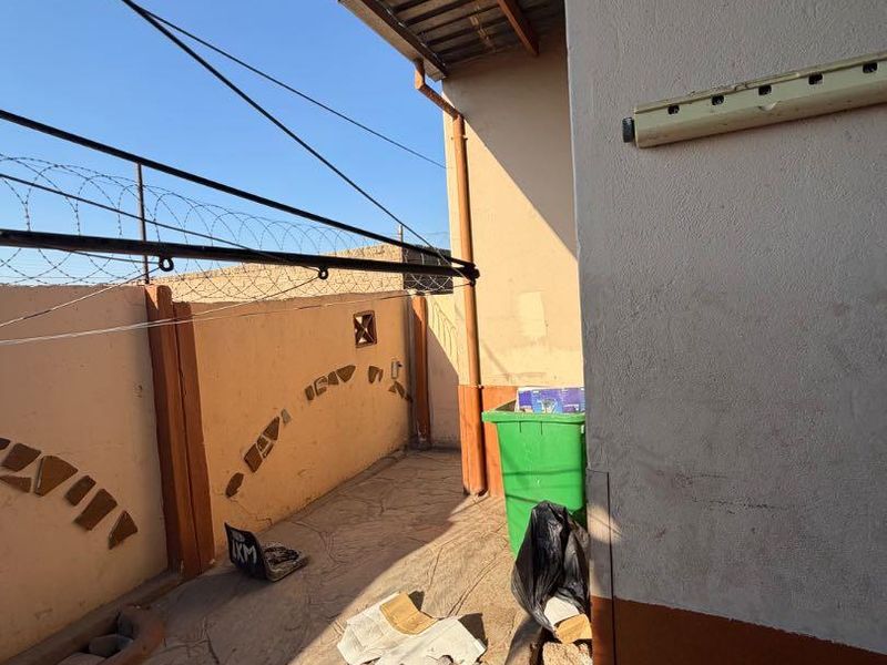 A narrow outdoor patio area featuring concrete paving, perimeter wall with security razor wire, and a covered roof structure.