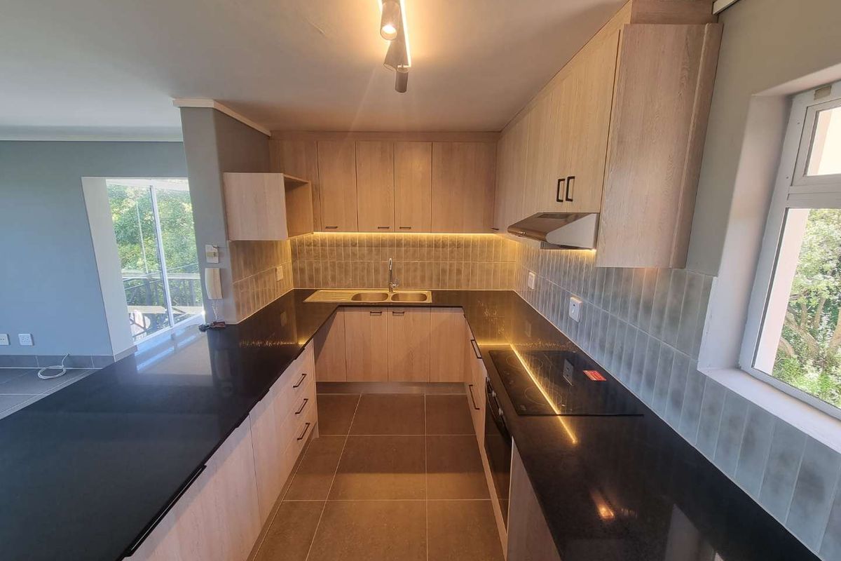Modern kitchen featuring light wood cabinetry, sleek black granite countertops, integrated appliances, and stylish under-cabinet lighting, creating a clean and functional workspace.