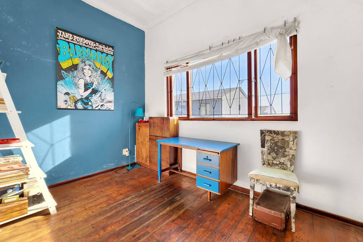 A bedroom featuring original timber flooring, large windows with security bars, and decorative ceiling cornicing.