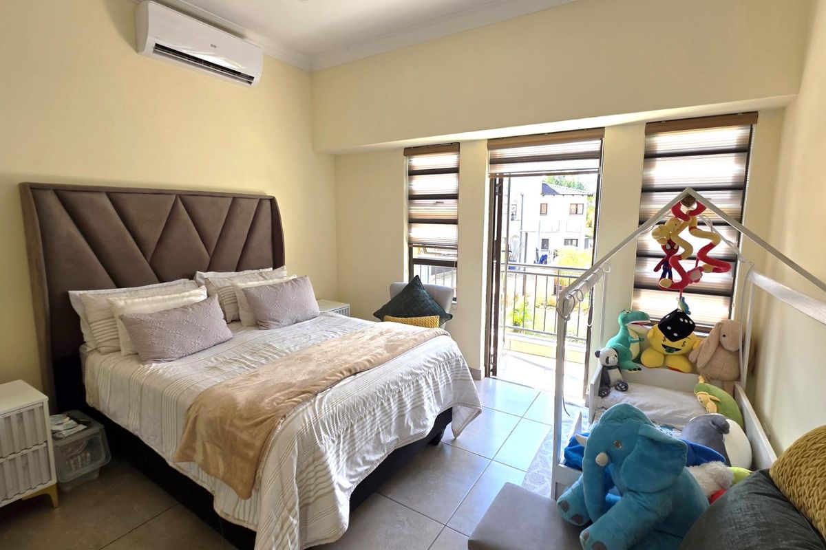 A well-lit bedroom featuring tiled flooring, a wall-mounted air conditioning unit, and a glass door providing access to a private balcony.