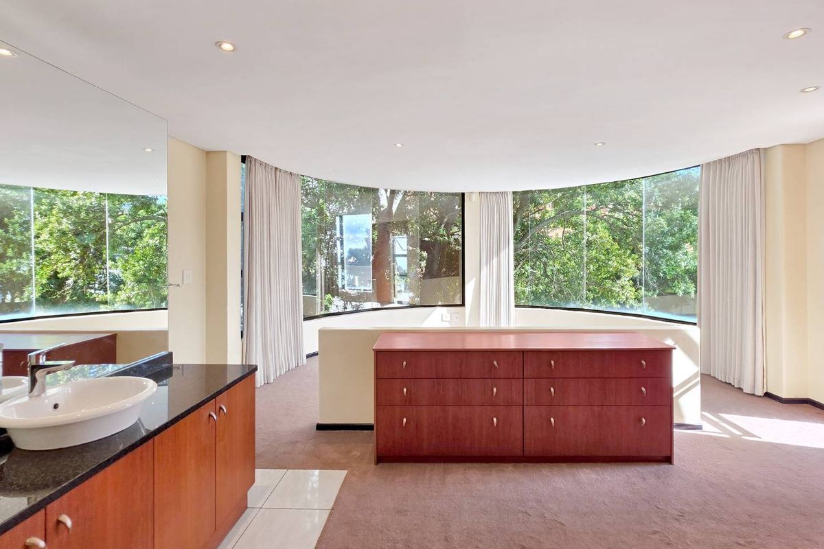 Spacious bedroom featuring a curved wall of windows, integrated vanity with basin, and neutral carpeting, offering a bright and open living space.