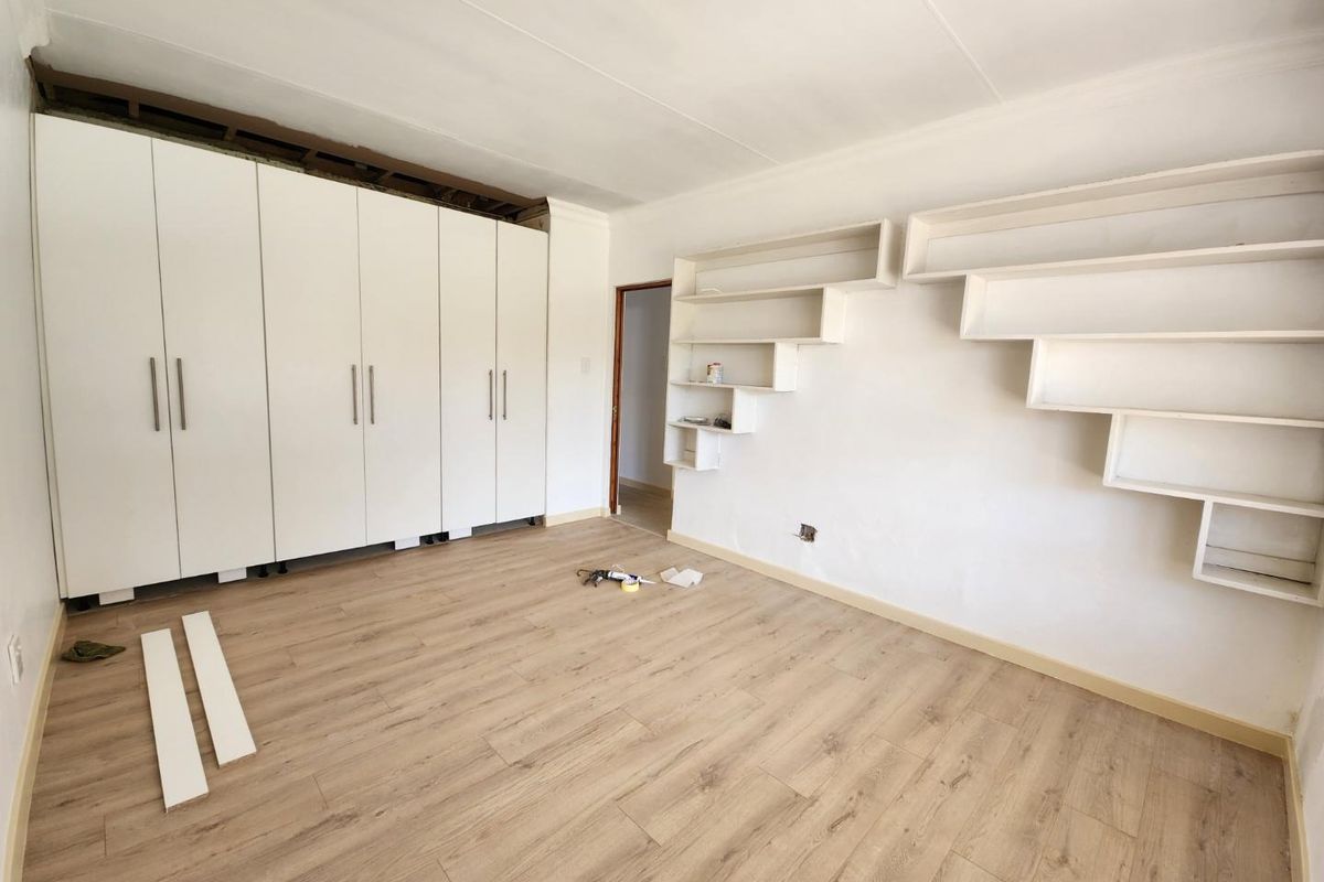 Bedroom featuring built-in white wardrobes and custom wall-mounted shelving, currently undergoing renovation with unfinished trim and flooring details.