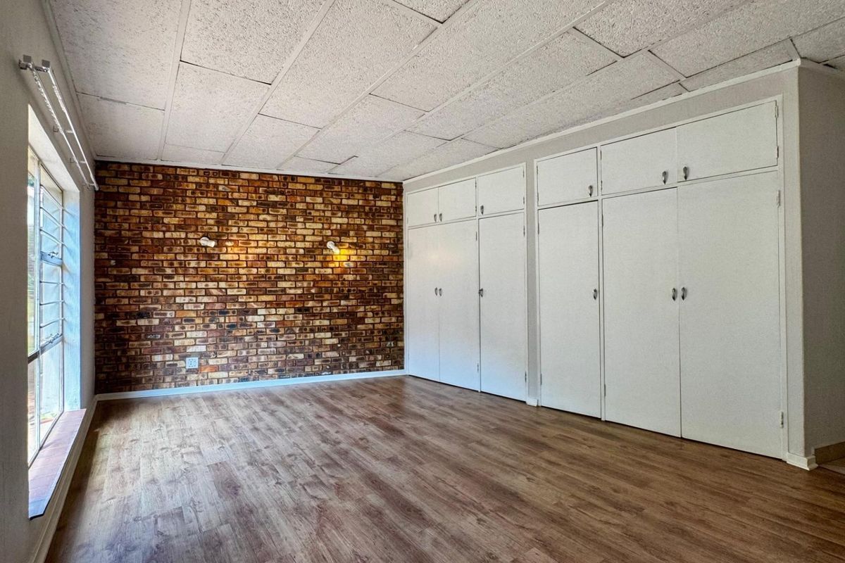 Spacious bedroom featuring an exposed brick accent wall, extensive built-in storage cupboards, and durable laminate flooring.