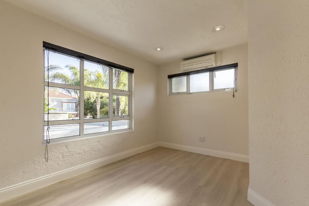 A bright, empty bedroom featuring light wood-look flooring, recessed ceiling lighting, and a wall-mounted air conditioning unit.