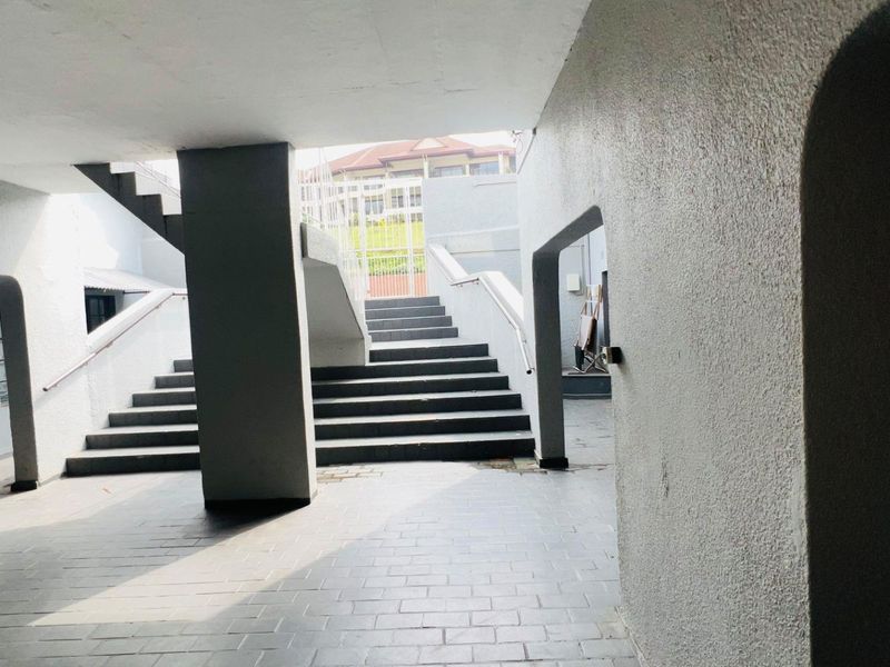 A covered outdoor entrance area featuring a concrete staircase with metal handrails and tiled flooring, providing access to the apartment complex.