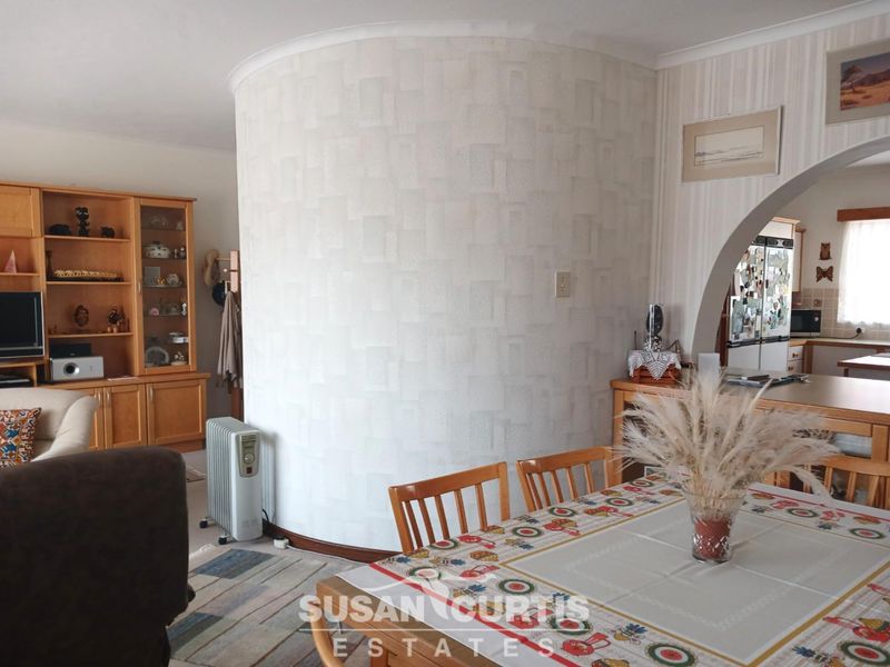 An open-plan living and dining area featuring a distinctive curved feature wall and an arched entryway leading into the kitchen space.