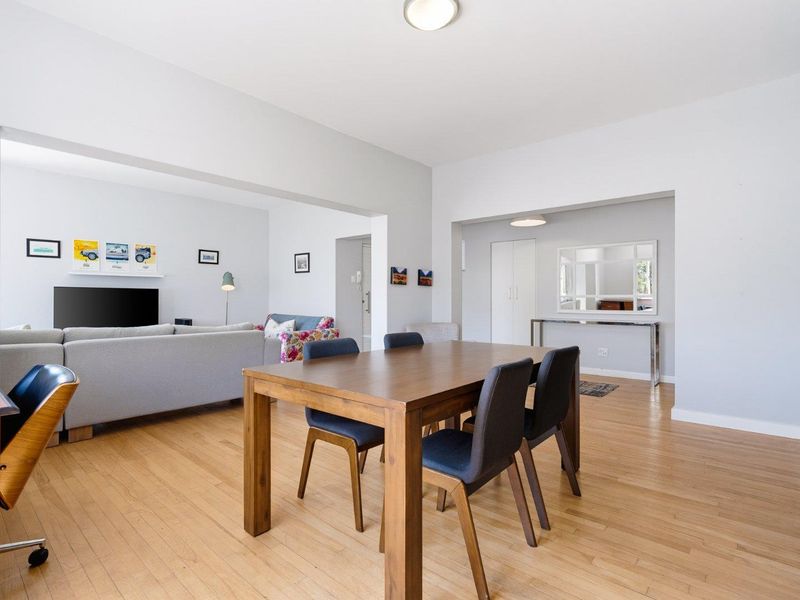 Spacious open-plan living and dining area featuring light hardwood flooring, neutral walls, and integrated storage, creating a bright and functional living space.