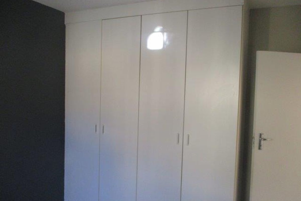 A bedroom featuring white built-in cupboards with a dark accent wall.