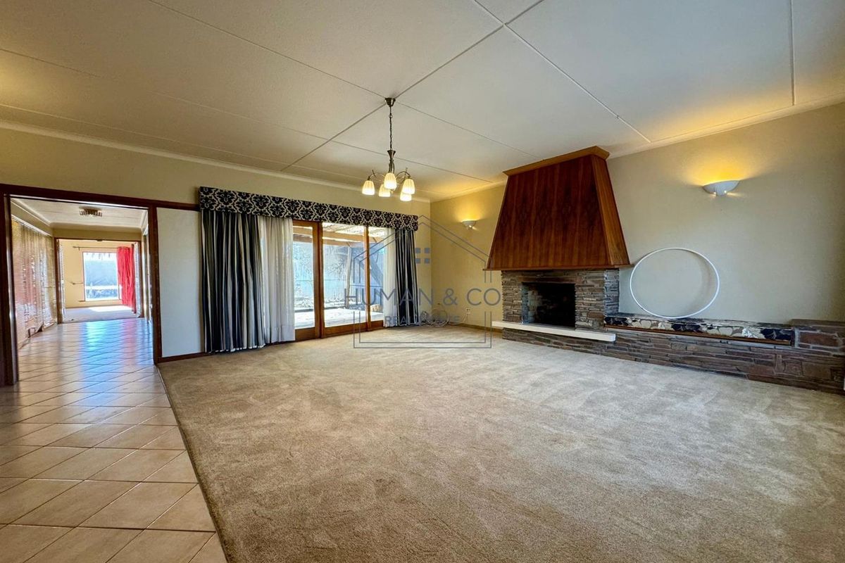 Spacious living room featuring a large stone fireplace with a wooden mantle, tiled entryway, and sliding glass doors leading to the patio.