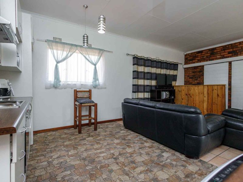 Open-plan living area featuring a functional kitchen with cabinetry, vinyl flooring, and an exposed brick feature wall, creating a versatile living space.