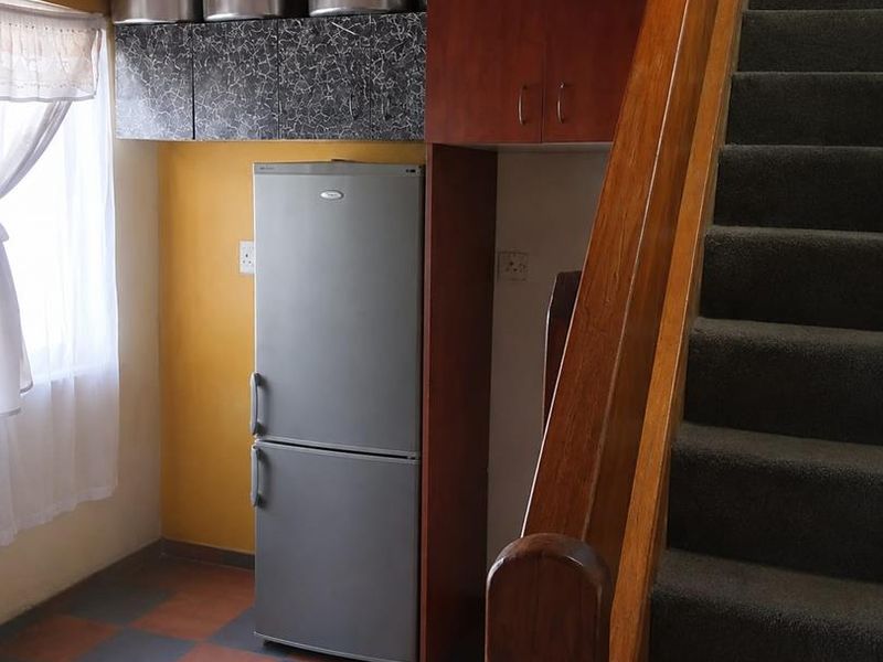A compact kitchen area featuring built-in cabinetry and tiled flooring, situated adjacent to a staircase with carpeted steps.