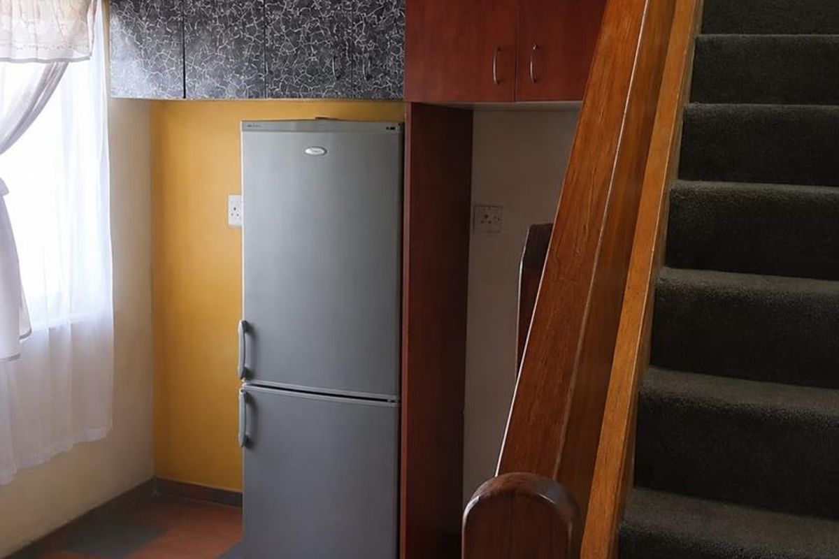 A compact kitchen area featuring built-in cabinetry and tiled flooring, situated adjacent to a staircase with carpeted steps.