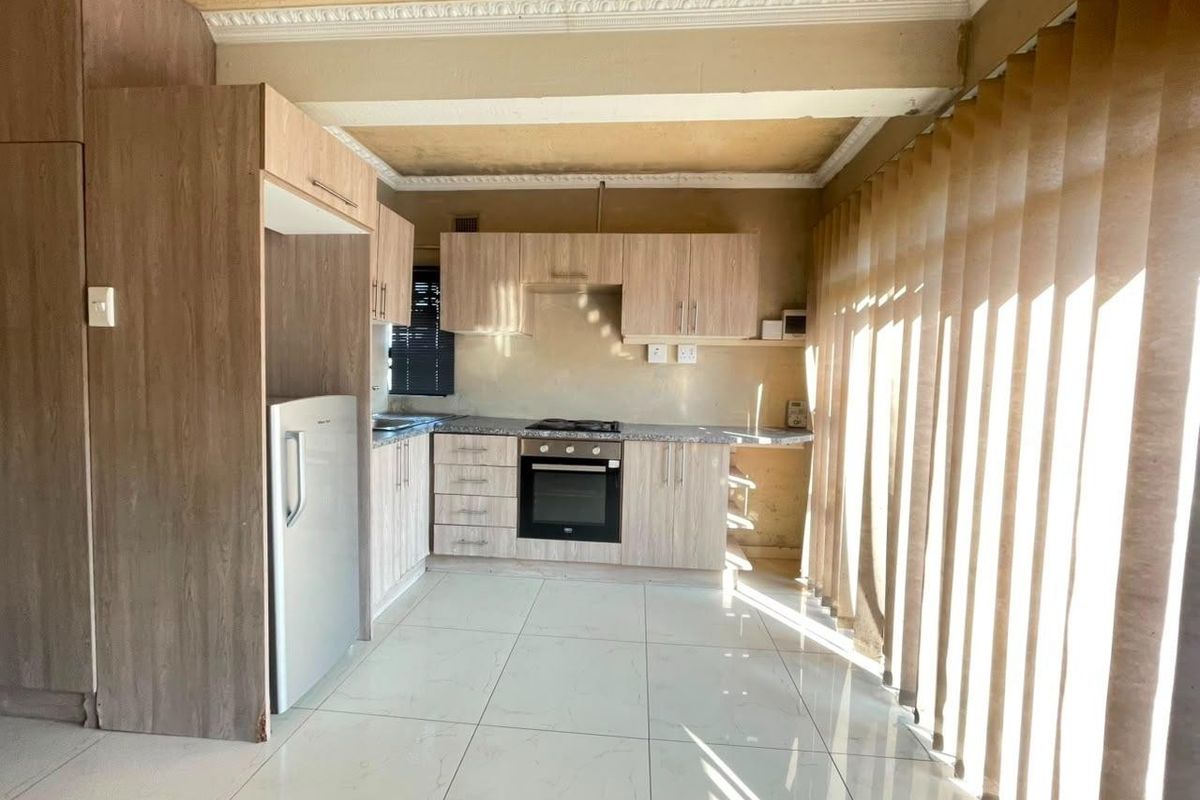 A functional kitchen featuring light wood-finish cabinetry, granite countertops, a built-in oven, and a gas hob, complemented by tiled flooring and decorative crown molding.