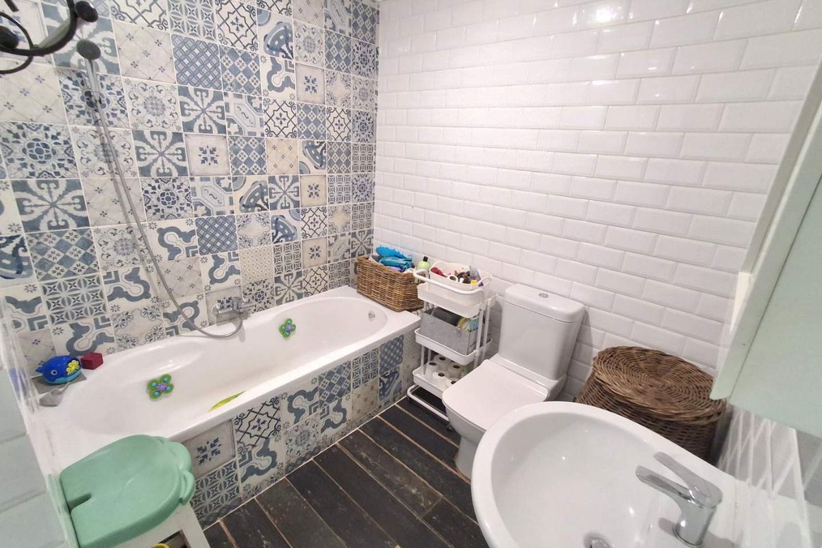 A bathroom featuring a bathtub with decorative patterned tiles, white subway wall tiles, a pedestal sink, and a toilet.