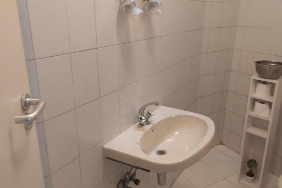 A compact bathroom featuring a wall-mounted basin with a chrome mixer tap, finished with neutral ceramic wall and floor tiles.