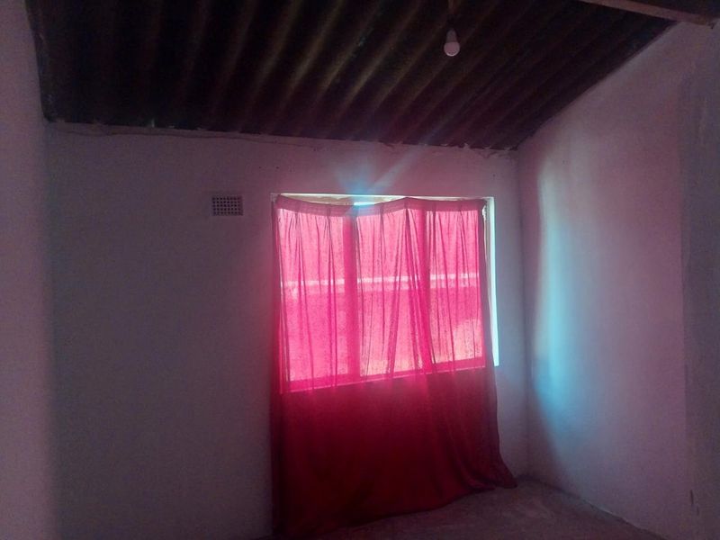 A basic, empty bedroom featuring a corrugated iron ceiling and a single ventilation brick, requiring significant cosmetic updates and finishing.