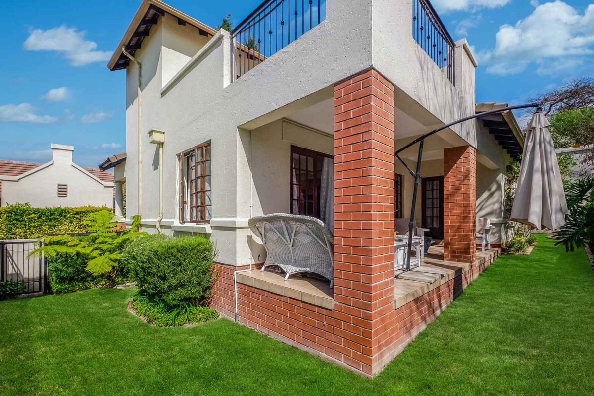 Rear view of the townhouse featuring a covered patio with brick pillars, a second-story balcony with metal railings, and a well-maintained garden.