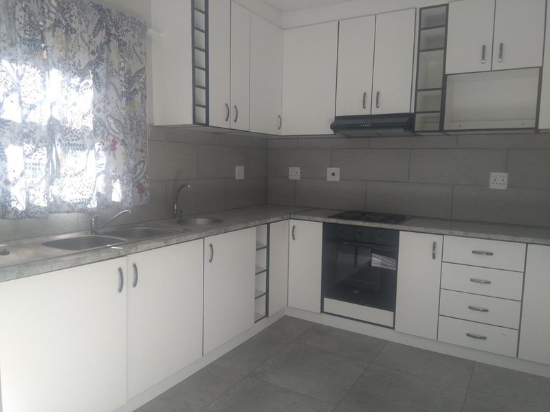 A clean, functional kitchen featuring white built-in cabinetry, grey tiled backsplash, laminate countertops, and integrated oven with hob.