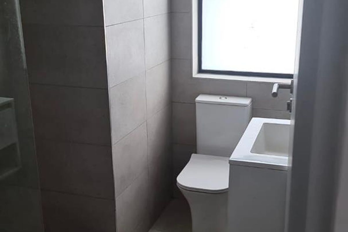 A modern, neutral-toned bathroom featuring a walk-in shower, a sleek vanity basin, and a toilet, finished with contemporary floor-to-ceiling tiling.