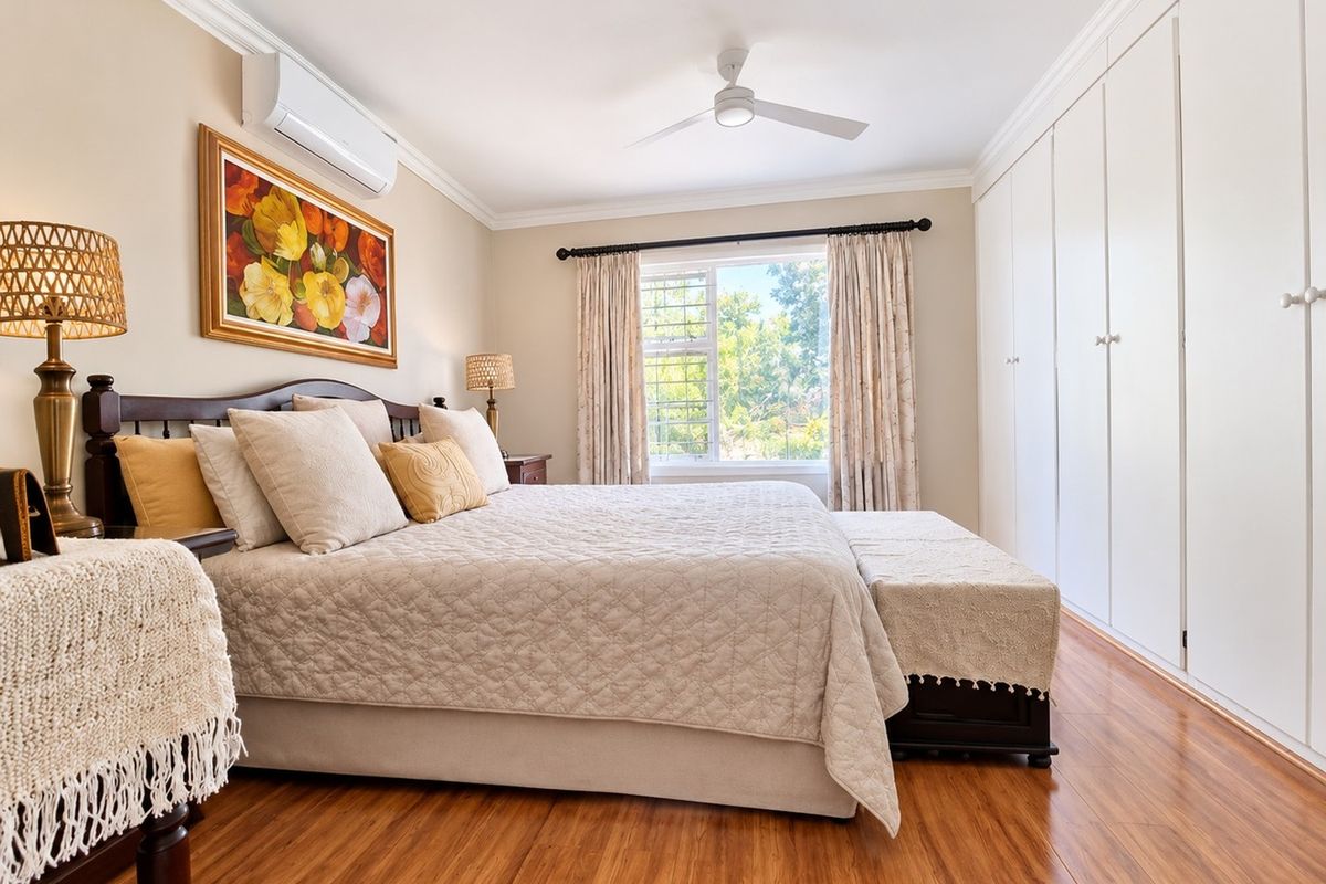 A well-maintained bedroom featuring laminate flooring, extensive built-in cupboards, a ceiling fan, and a wall-mounted air conditioning unit.