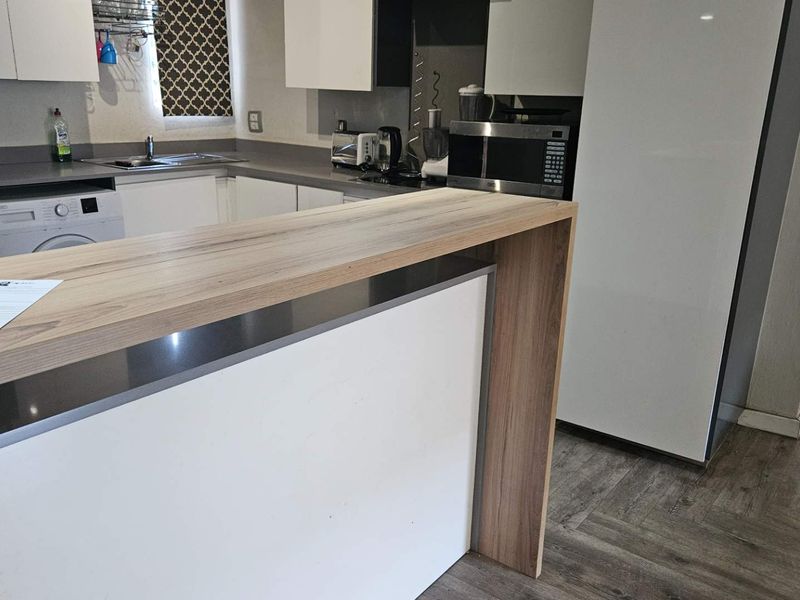 Modern kitchen featuring a wood-look breakfast bar, white cabinetry, integrated appliances, and durable wood-effect flooring.
