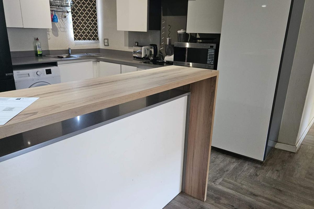 Modern kitchen featuring a wood-look breakfast bar, white cabinetry, integrated appliances, and durable wood-effect flooring.