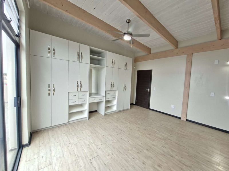 Spacious bedroom featuring extensive built-in cabinetry, exposed timber ceiling beams, a ceiling fan, and modern laminate flooring with access to a sliding glass door.