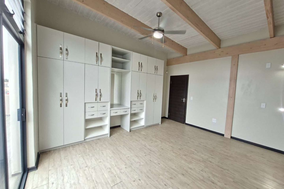 Spacious bedroom featuring extensive built-in cabinetry, exposed timber ceiling beams, a ceiling fan, and modern laminate flooring with access to a sliding glass door.