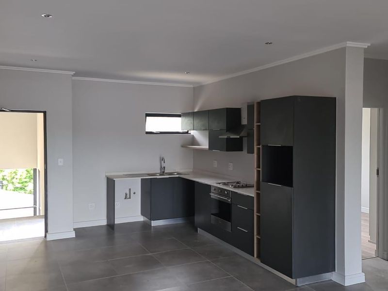Modern open-plan kitchen featuring sleek dark cabinetry, stone countertops, integrated oven and hob, and neutral tiled flooring in a well-lit space.
