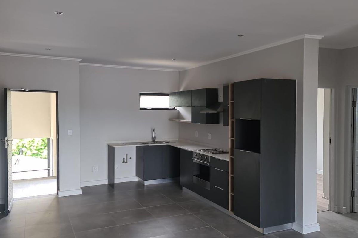 Modern open-plan kitchen featuring sleek dark cabinetry, stone countertops, integrated oven and hob, and neutral tiled flooring in a well-lit space.