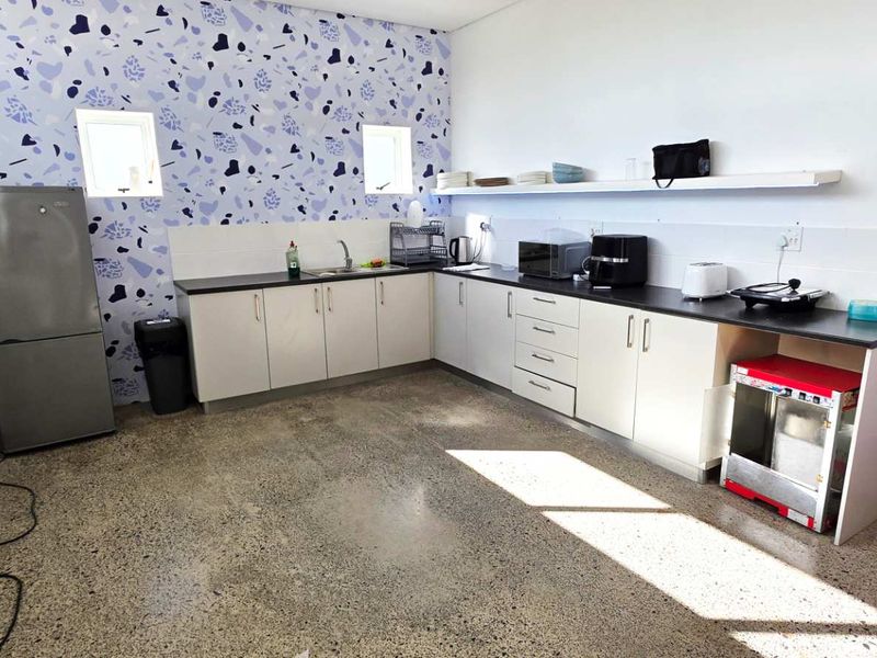 A functional kitchen area featuring L-shaped cabinetry, polished concrete flooring, and a decorative patterned feature wall with integrated sink and countertop space.