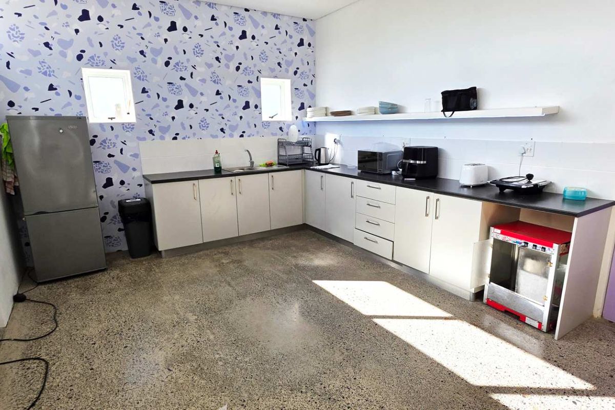 A functional kitchen area featuring L-shaped cabinetry, polished concrete flooring, and a decorative patterned feature wall with integrated sink and countertop space.
