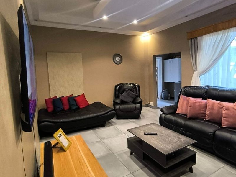 A comfortable living room featuring large format floor tiles, recessed ceiling lighting with a coved design, and neutral wall tones.