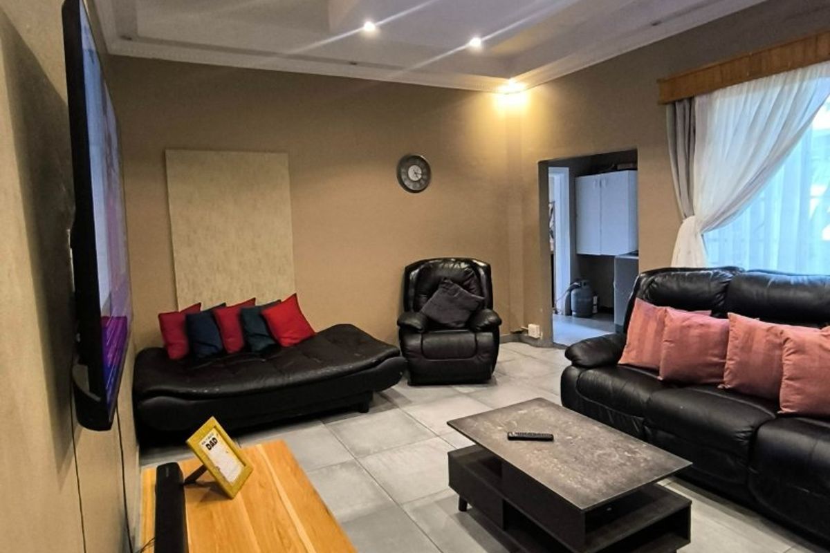 A comfortable living room featuring large format floor tiles, recessed ceiling lighting with a coved design, and neutral wall tones.