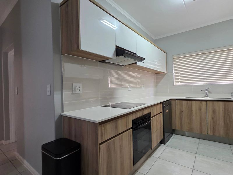 Modern kitchen featuring wood-grain cabinetry, white countertops, integrated oven and hob, tiled backsplash, and neutral floor tiles.