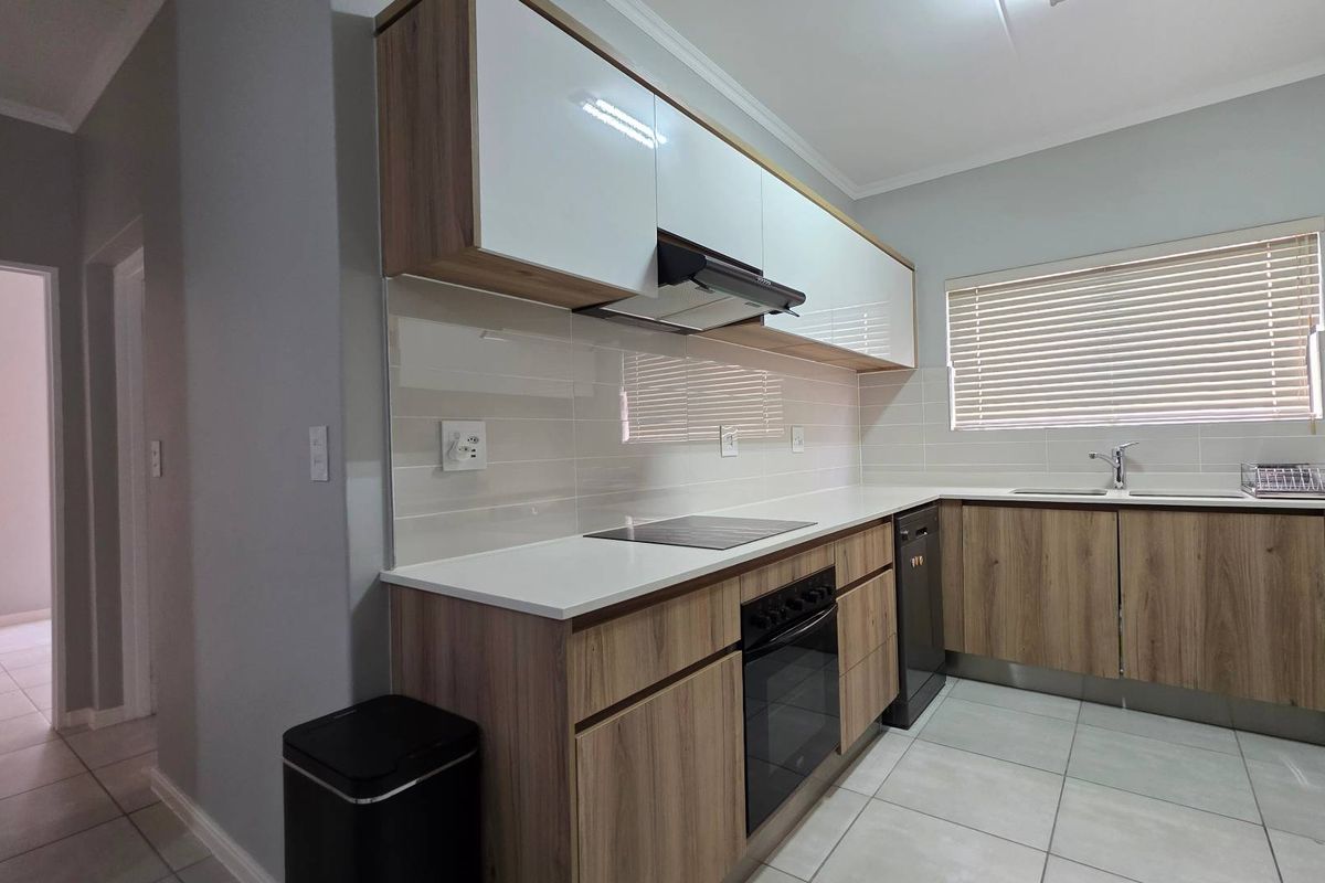 Modern kitchen featuring wood-grain cabinetry, white countertops, integrated oven and hob, tiled backsplash, and neutral floor tiles.