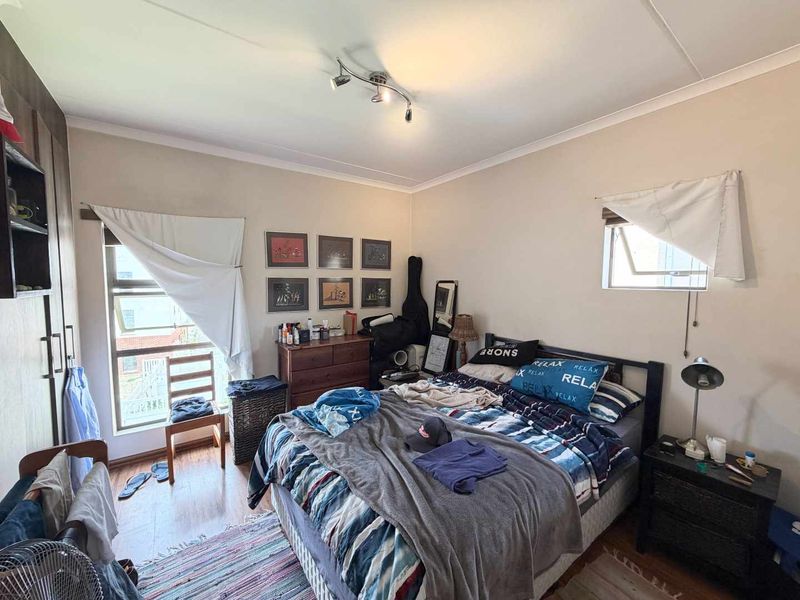 A functional bedroom featuring built-in cupboards, laminate flooring, and natural light from top-hung windows.