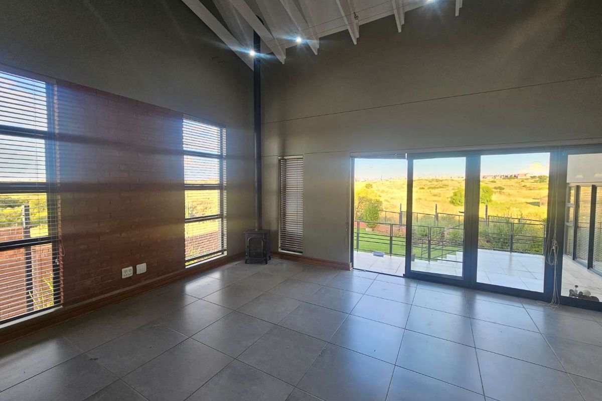 Spacious living area featuring high vaulted ceilings, exposed brick feature wall, tiled flooring, a built-in fireplace, and large sliding doors opening to a patio.