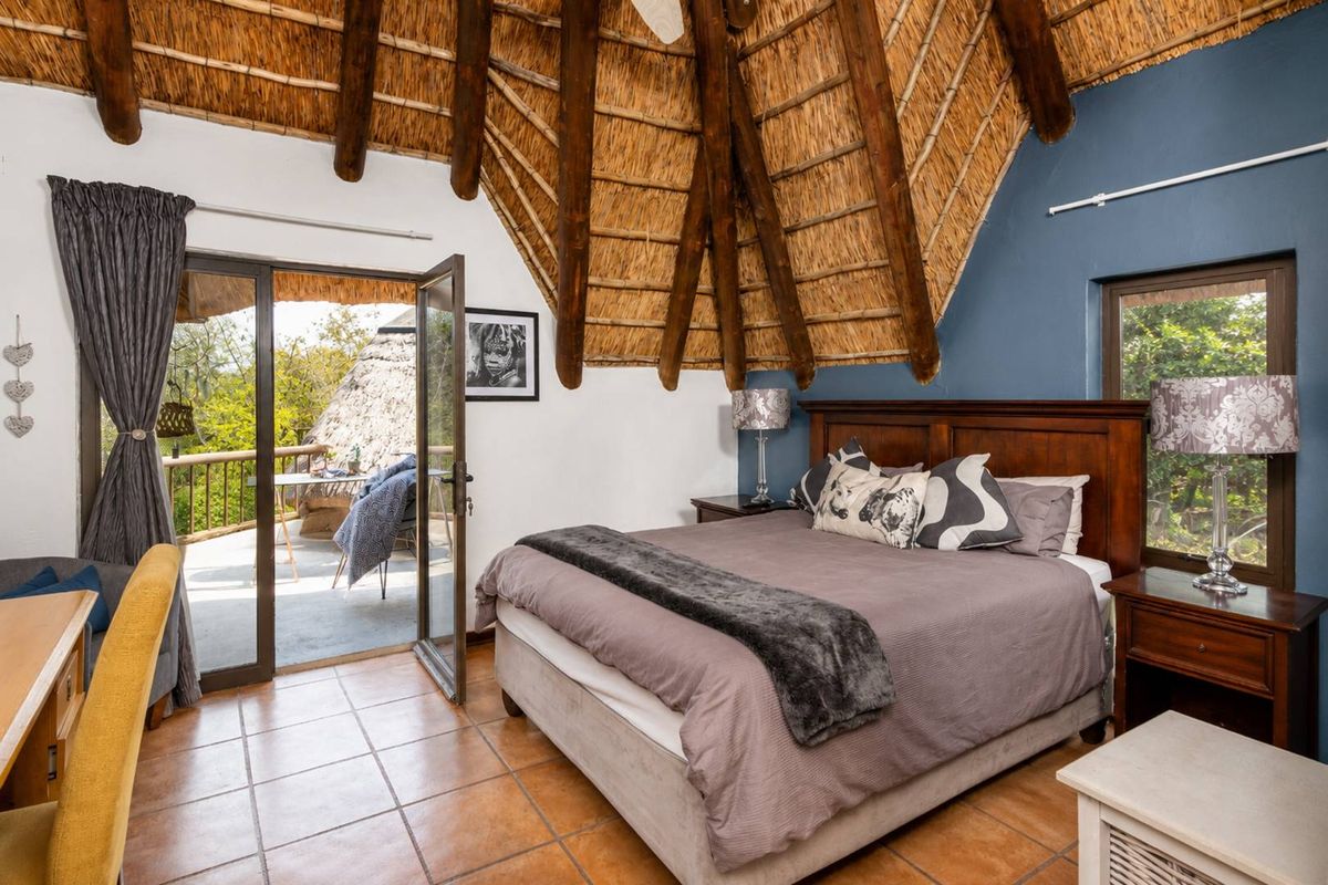 A bedroom featuring a high thatched ceiling with exposed timber rafters, tiled flooring, and direct access to an outdoor balcony through glass sliding doors.