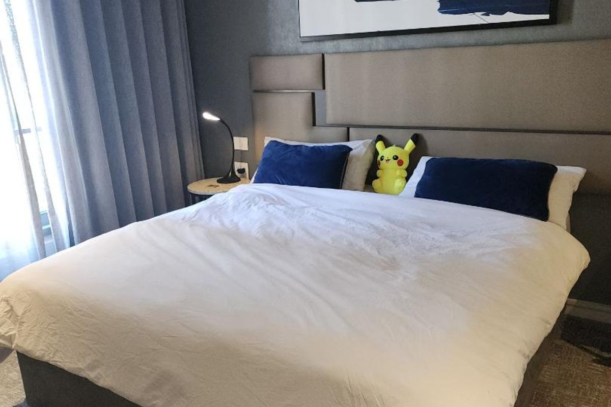 A well-appointed bedroom featuring a modern upholstered headboard, neutral carpeting, and floor-to-ceiling curtains providing natural light.