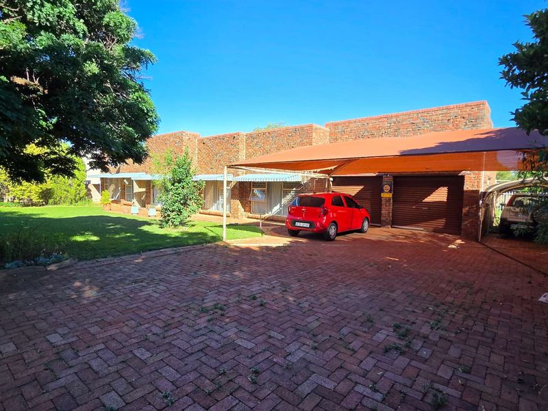 Front view of a face brick house featuring a paved driveway, double garage with shade cloth carport, and a well-maintained garden area.