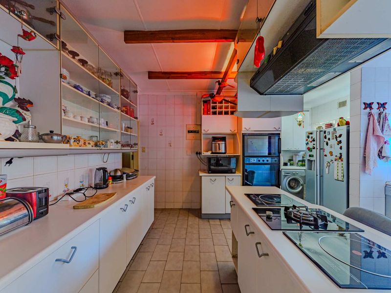 A functional kitchen featuring white cabinetry, a central island with a built-in hob, exposed ceiling beams, and tiled finishes throughout.
