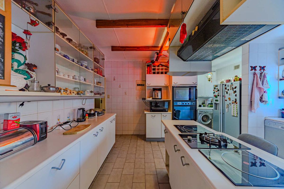 A functional kitchen featuring white cabinetry, a central island with a built-in hob, exposed ceiling beams, and tiled finishes throughout.
