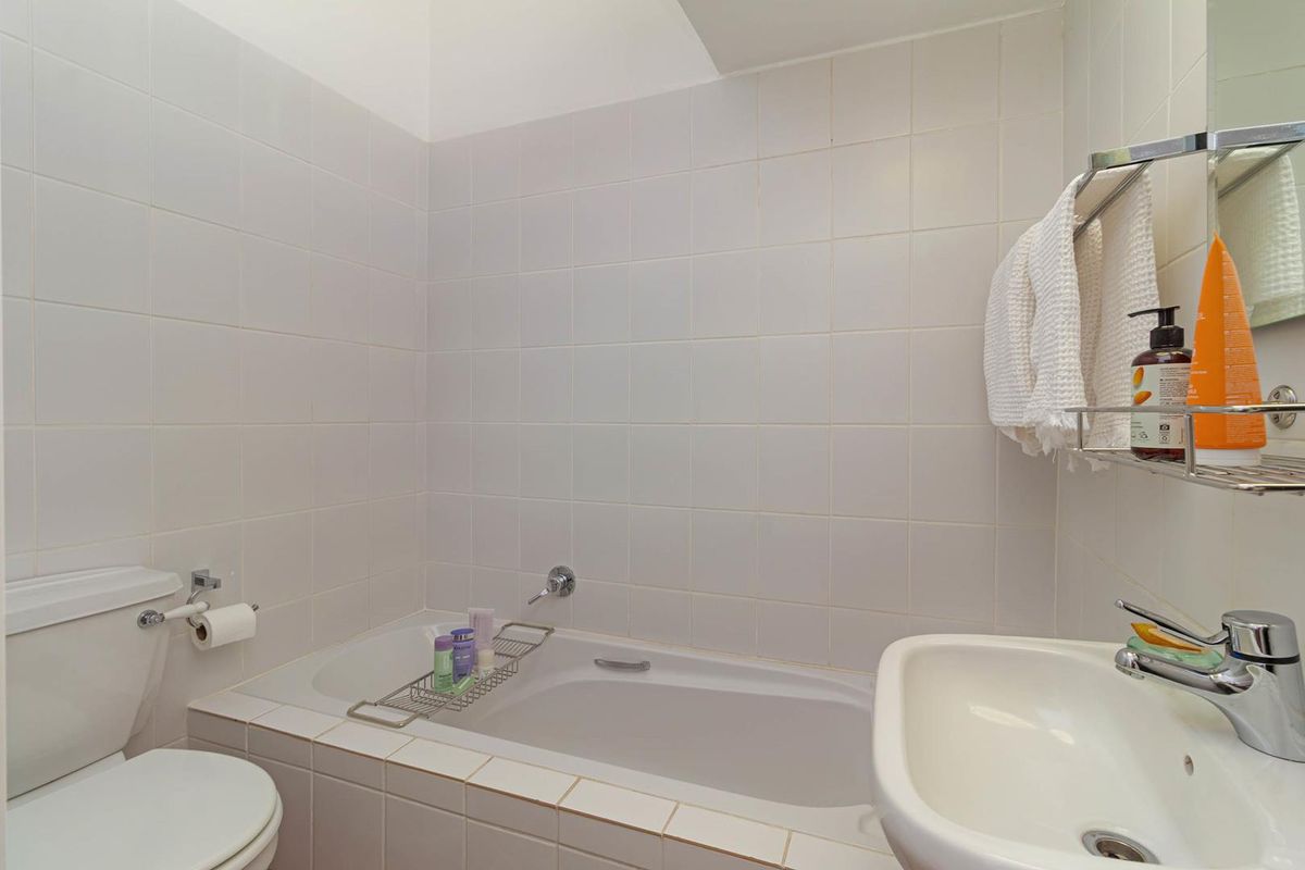 A functional bathroom featuring a built-in bathtub, white ceramic wall tiling, a standard toilet, and a wall-mounted washbasin with chrome fixtures.