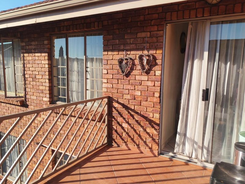 A private balcony featuring exposed brickwork, tiled flooring, and a metal balustrade, providing direct access to the interior through a sliding glass door.