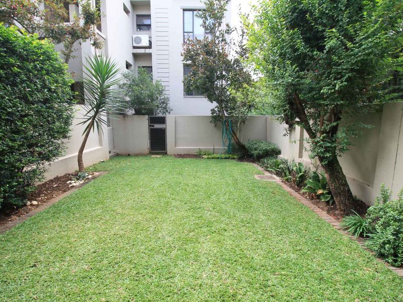 A private, well-maintained garden area featuring a central lawn, mature trees, and perimeter boundary walls.
