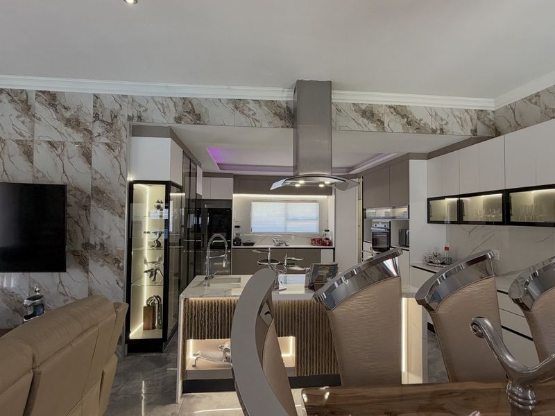 Modern open-plan living and kitchen area featuring high-end marble-effect wall finishes, sleek cabinetry, integrated lighting, and a central kitchen island with a stainless steel extractor.