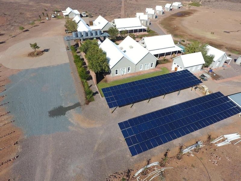 Aerial view of a farm property featuring multiple buildings with metal roofs, extensive solar panel arrays, and water storage infrastructure.