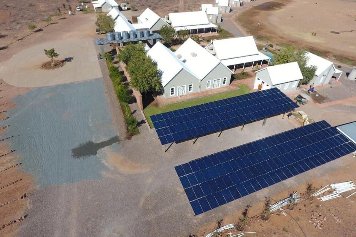 Aerial view of a farm property featuring multiple buildings with metal roofs, extensive solar panel arrays, and water storage infrastructure.